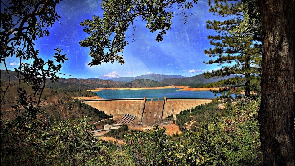 A dam with a reservoir, surrounded by mountains and trees.