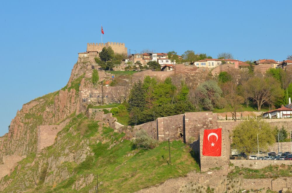 A hilltop with a castle, a Turkish flag, and residential buildings.