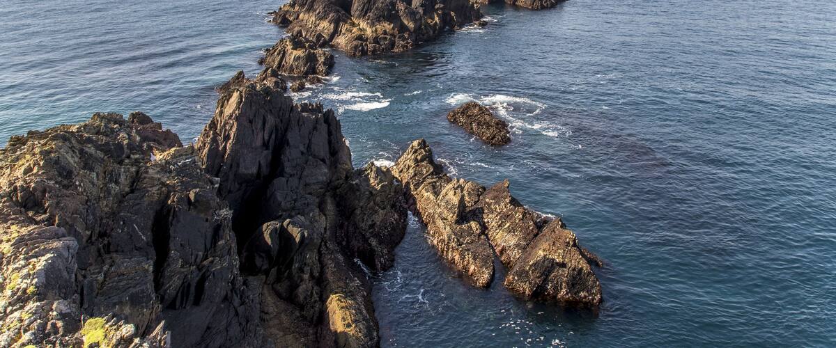 A rocky coastline with a prominent hill covered in grass and a distant green hill.