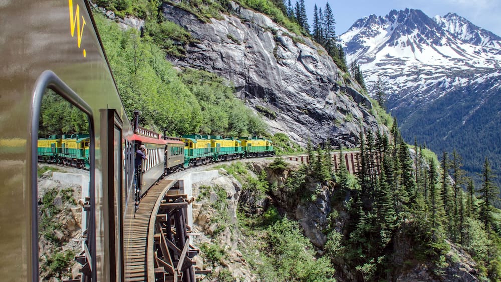 A train on a mountain track with snow-capped mountains in the background.