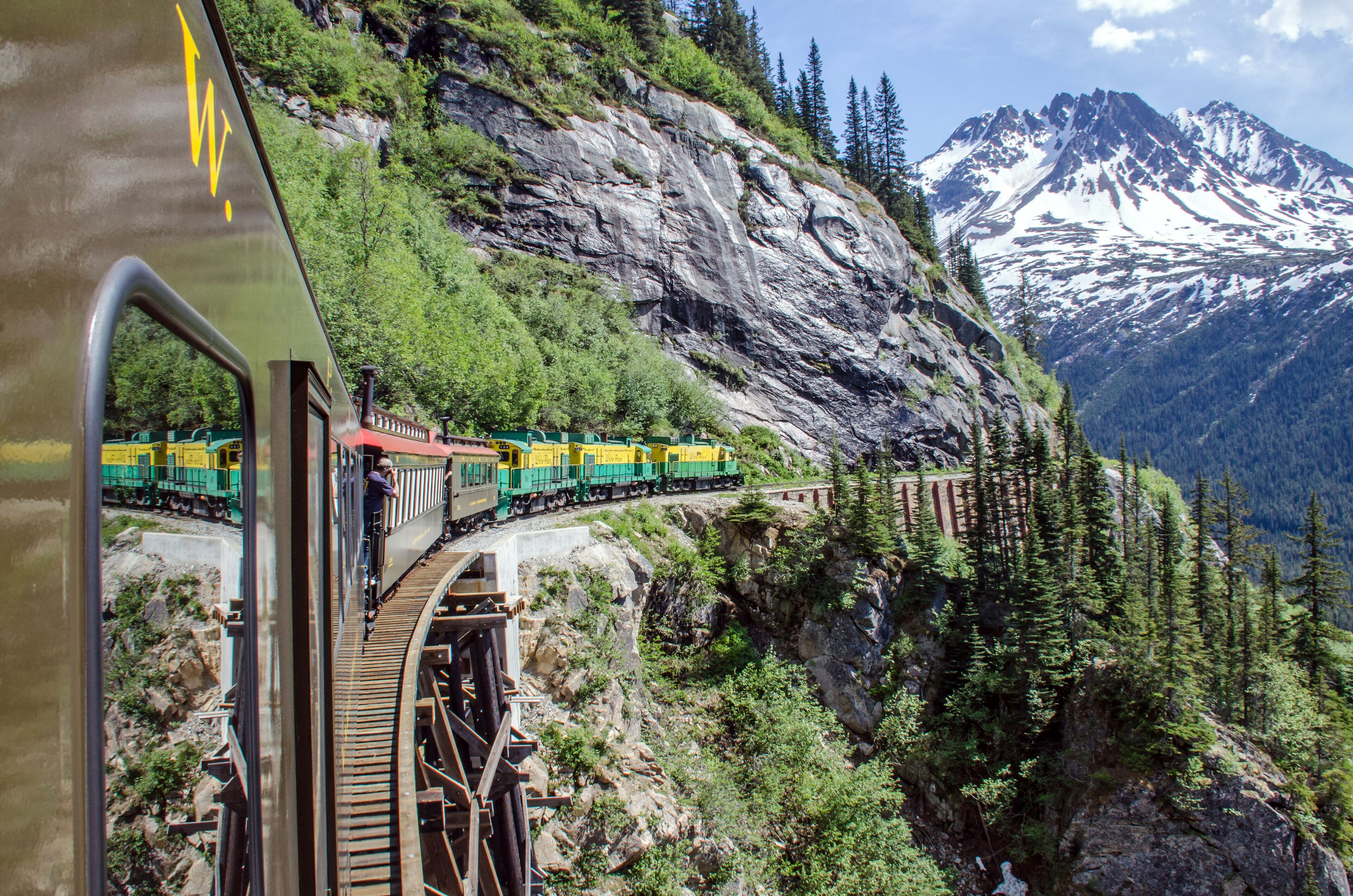 A train on a mountain track with snow-capped mountains in the background.