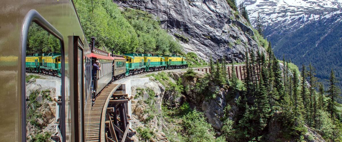 A train on a mountain track with snow-capped mountains in the background.