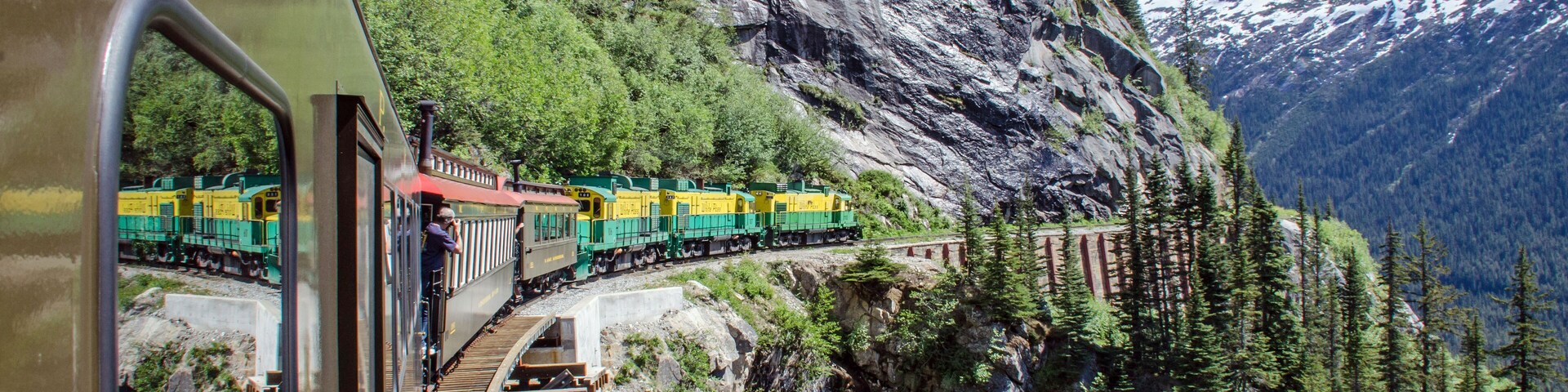 A train on a mountain track with snow-capped mountains in the background.