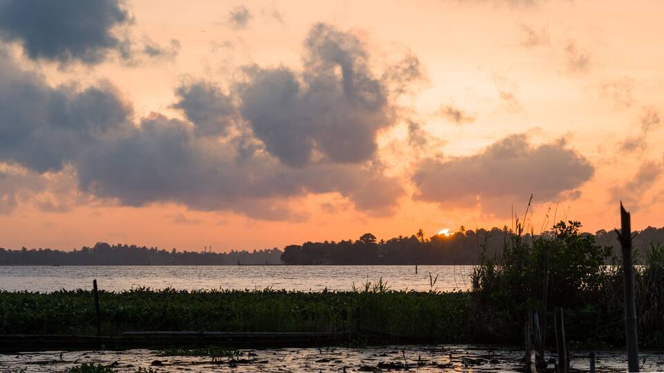A sunset over a body of water with a distant shoreline and vegetation.