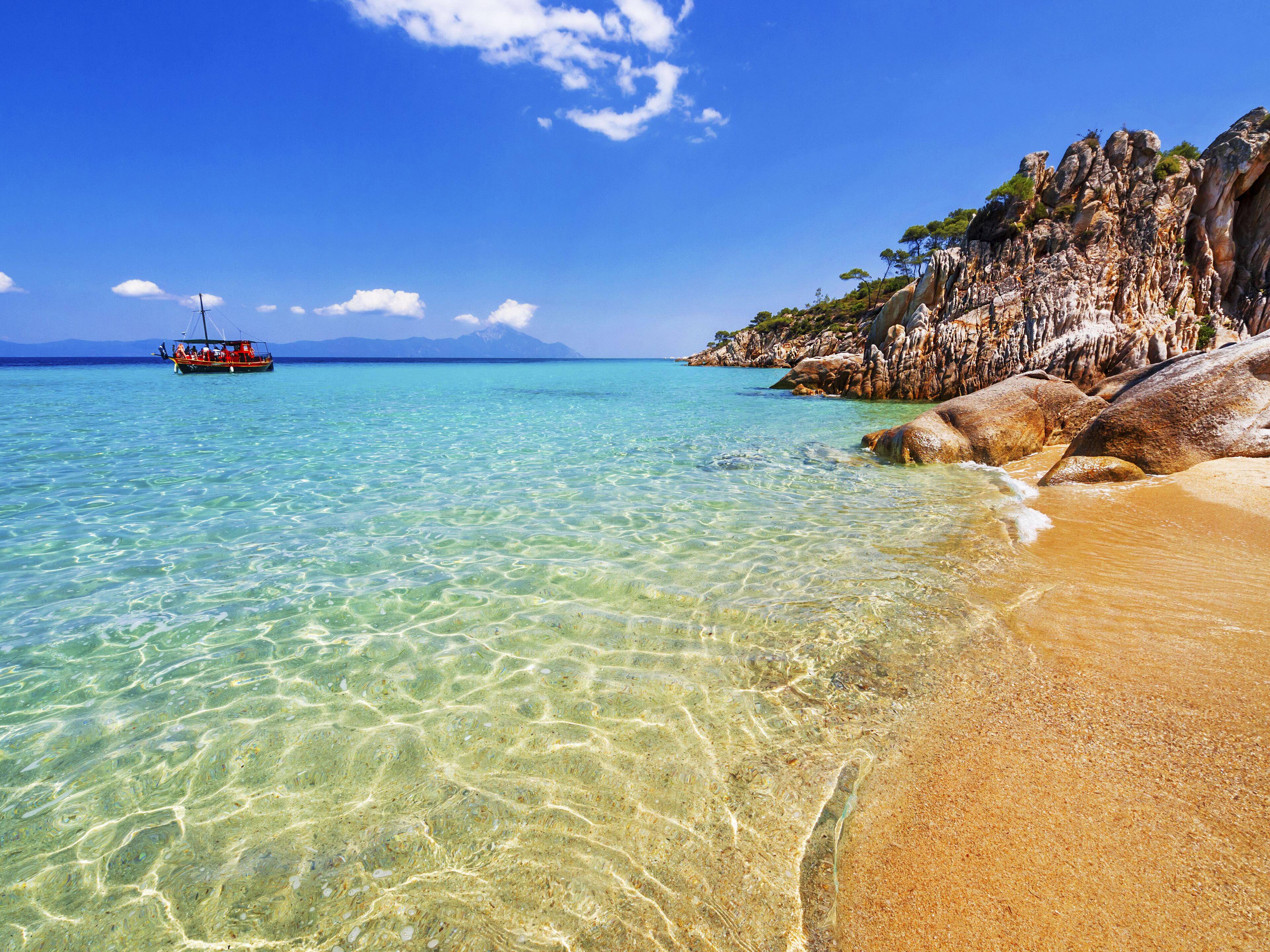 A clear turquoise sea, a sandy beach, and rocky cliffs with sparse vegetation.