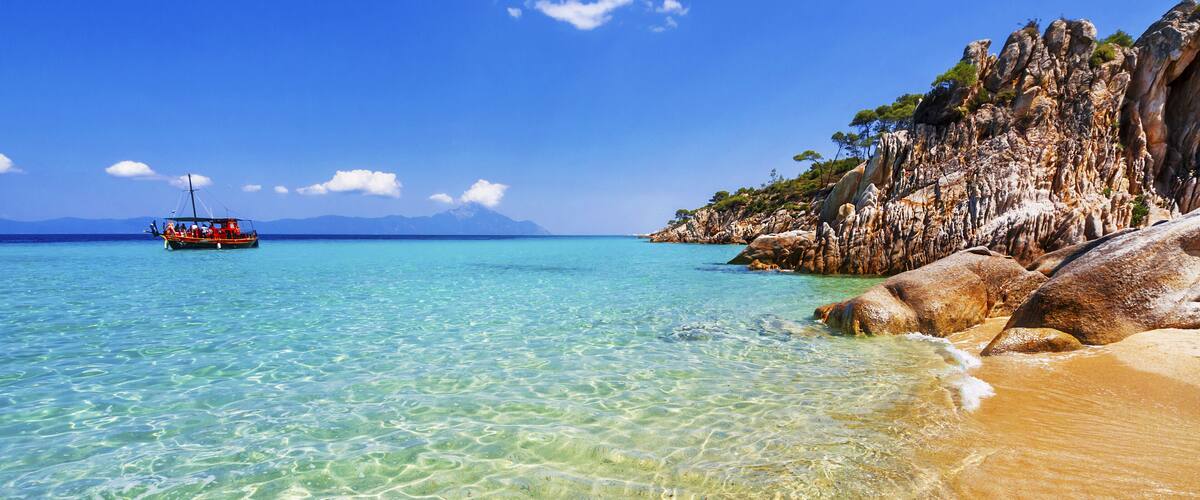 A clear turquoise sea, a sandy beach, and rocky cliffs with sparse vegetation.