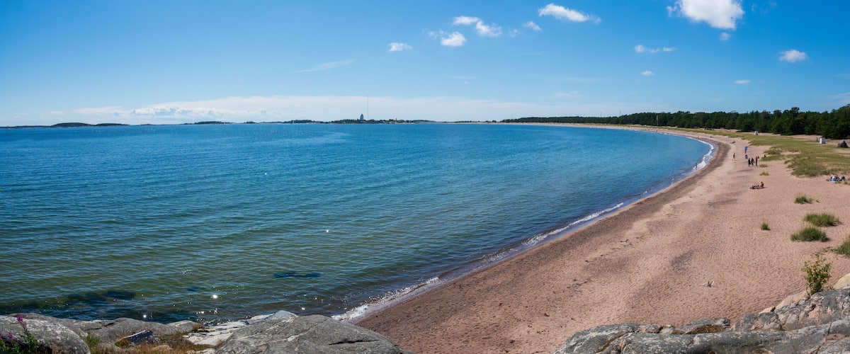 A sandy beach with calm waters, a clear sky, and distant landforms.