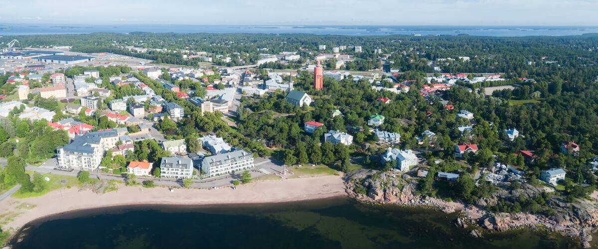 An aerial view of a coastal town with a beach, dense forest, and various buildings.