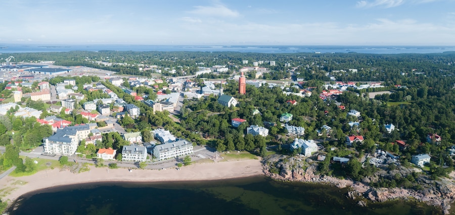 An aerial view of a coastal town with a beach, dense forest, and various buildings.