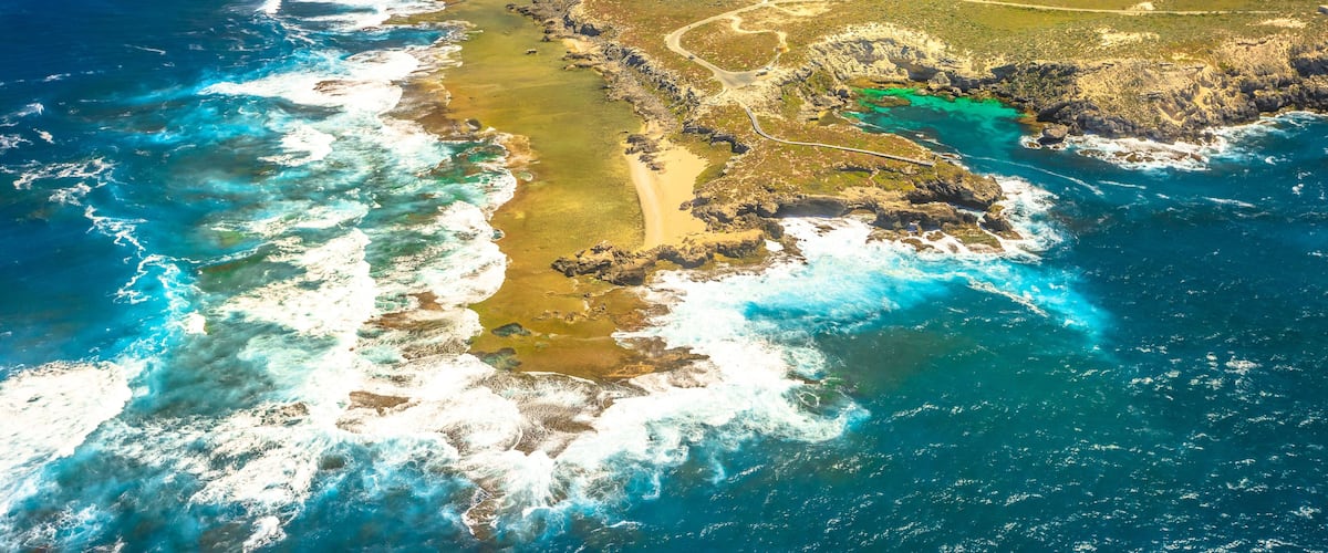 An aerial view of a coastal landscape with rocky shores, clear blue waters, and a winding road along the coastline.