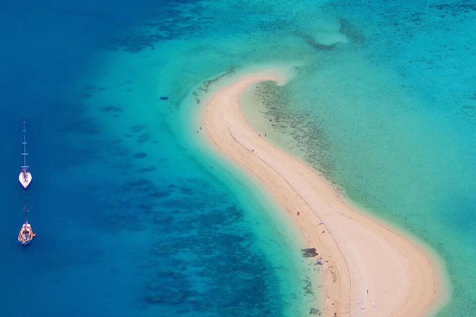 Una vista aerea di una spiaggia sabbiosa che si incurva, con acque cristalline color turchese.