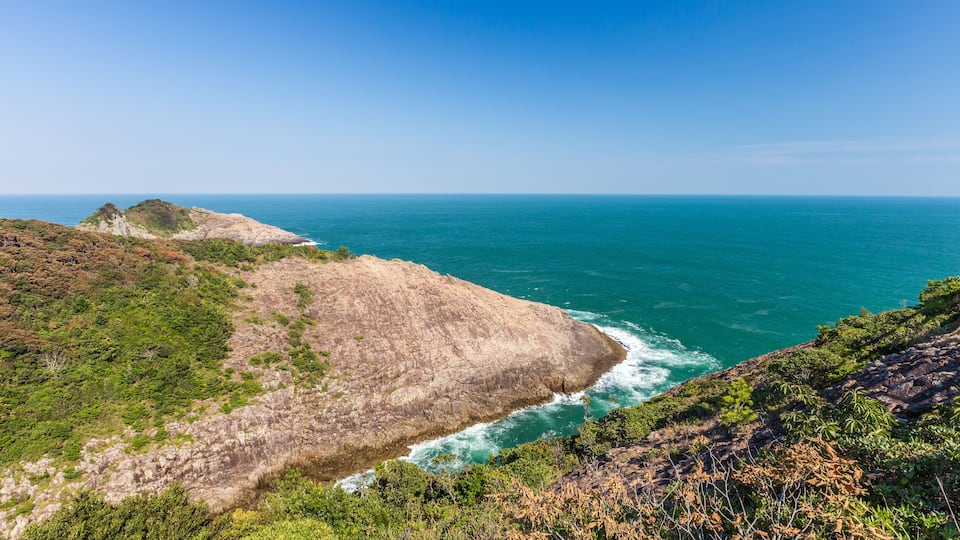 A coastal landscape with rocky cliffs and a clear blue sea.