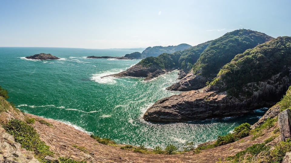 A coastal landscape with rocky cliffs, a clear blue sea, and lush greenery.