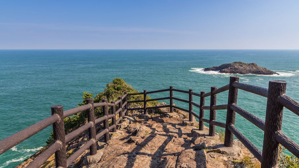 A wooden staircase leading to a viewpoint overlooking the ocean with a rocky island in the distance.
