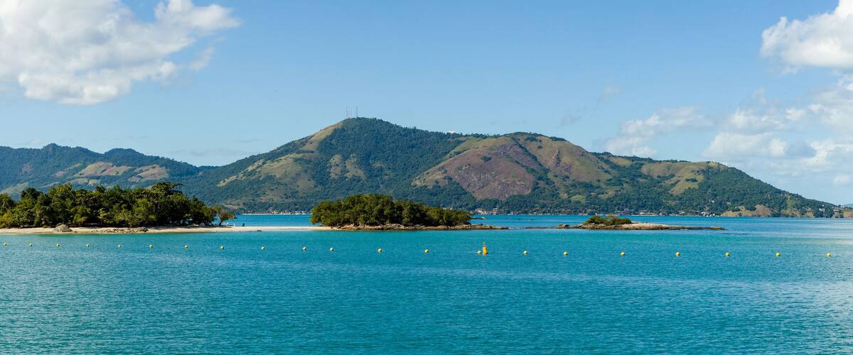 A coastal landscape with clear turquoise waters, sandy beaches, and lush green hills in the background.
