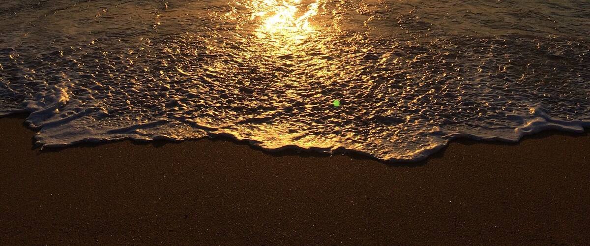 A sunset over the ocean with waves reflecting the sun's light on the beach.