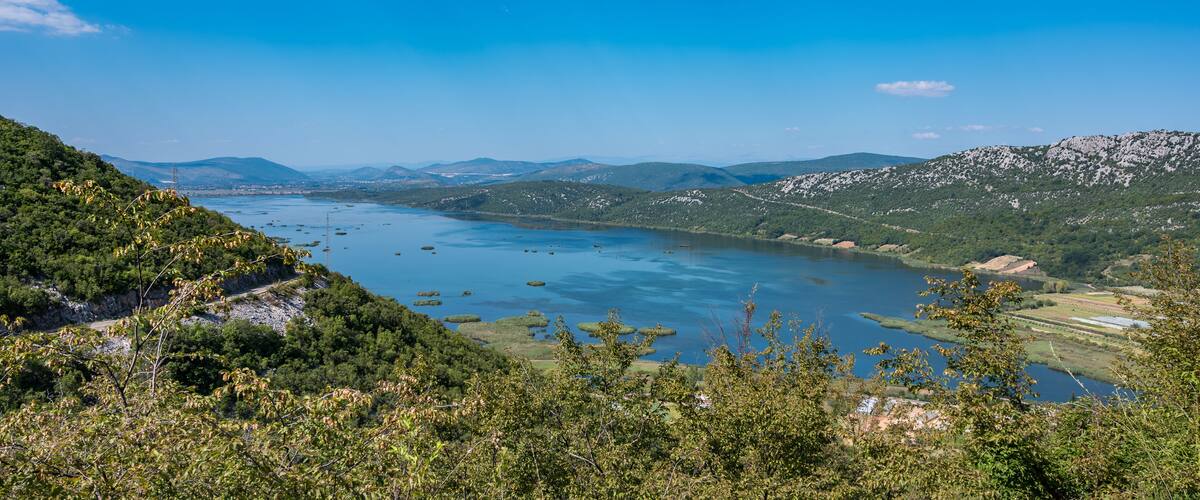 A mountainous landscape with a lake surrounded by greenery and distant mountains.