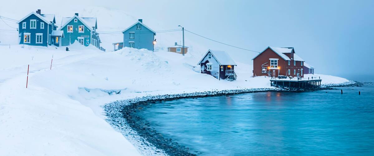 A snow-covered coastal village with houses by the sea.