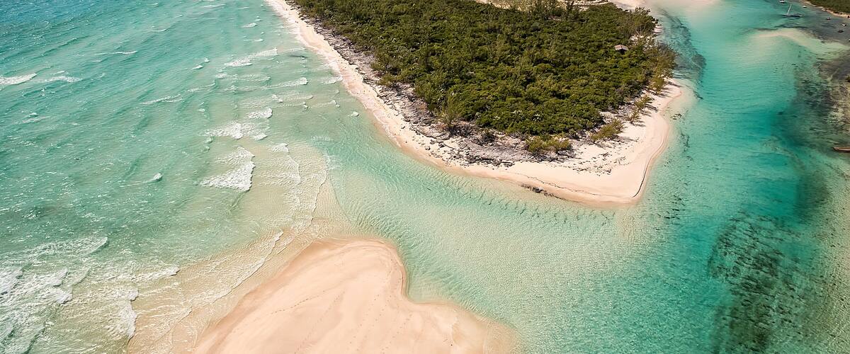 An aerial view of a coastal area with turquoise waters, a sandy beach, and a dense forested island.