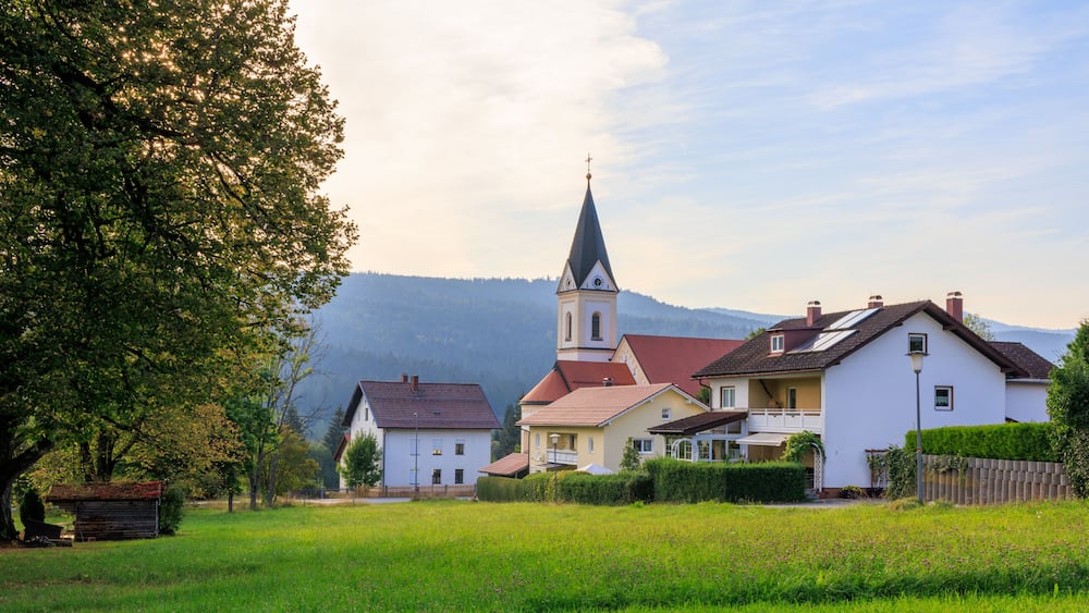 A church with a steeple, a white house, and a green field with a tree.