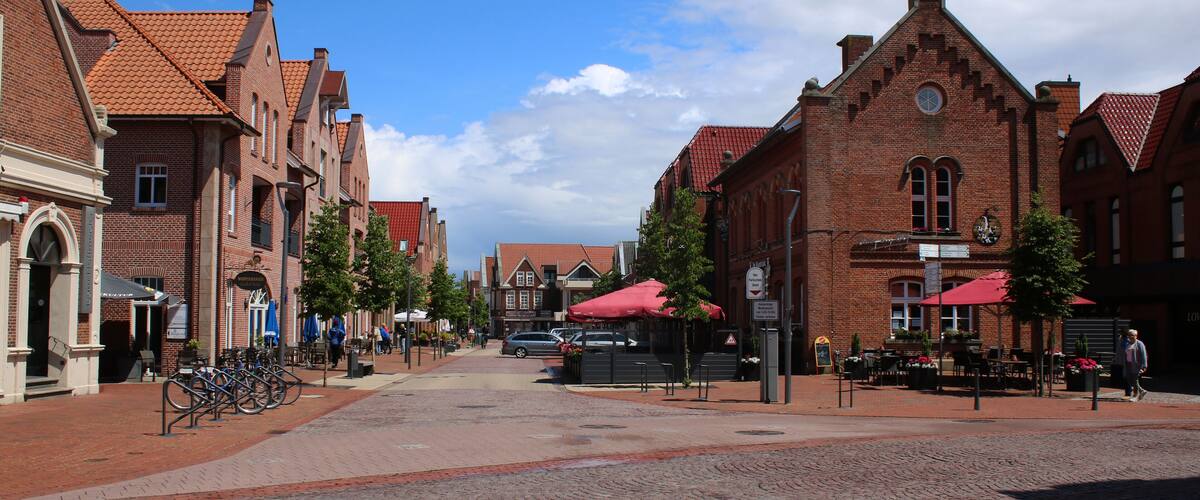 A cobblestone street lined with historic brick buildings, red awnings, and a clear blue sky.