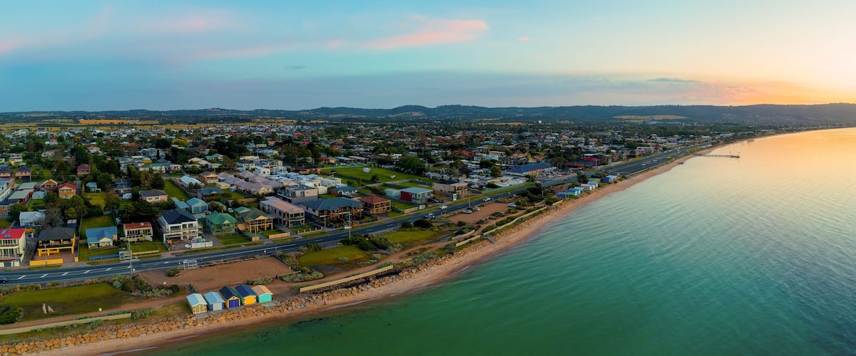 A coastal town with a beach, houses, and a road along the shoreline.
