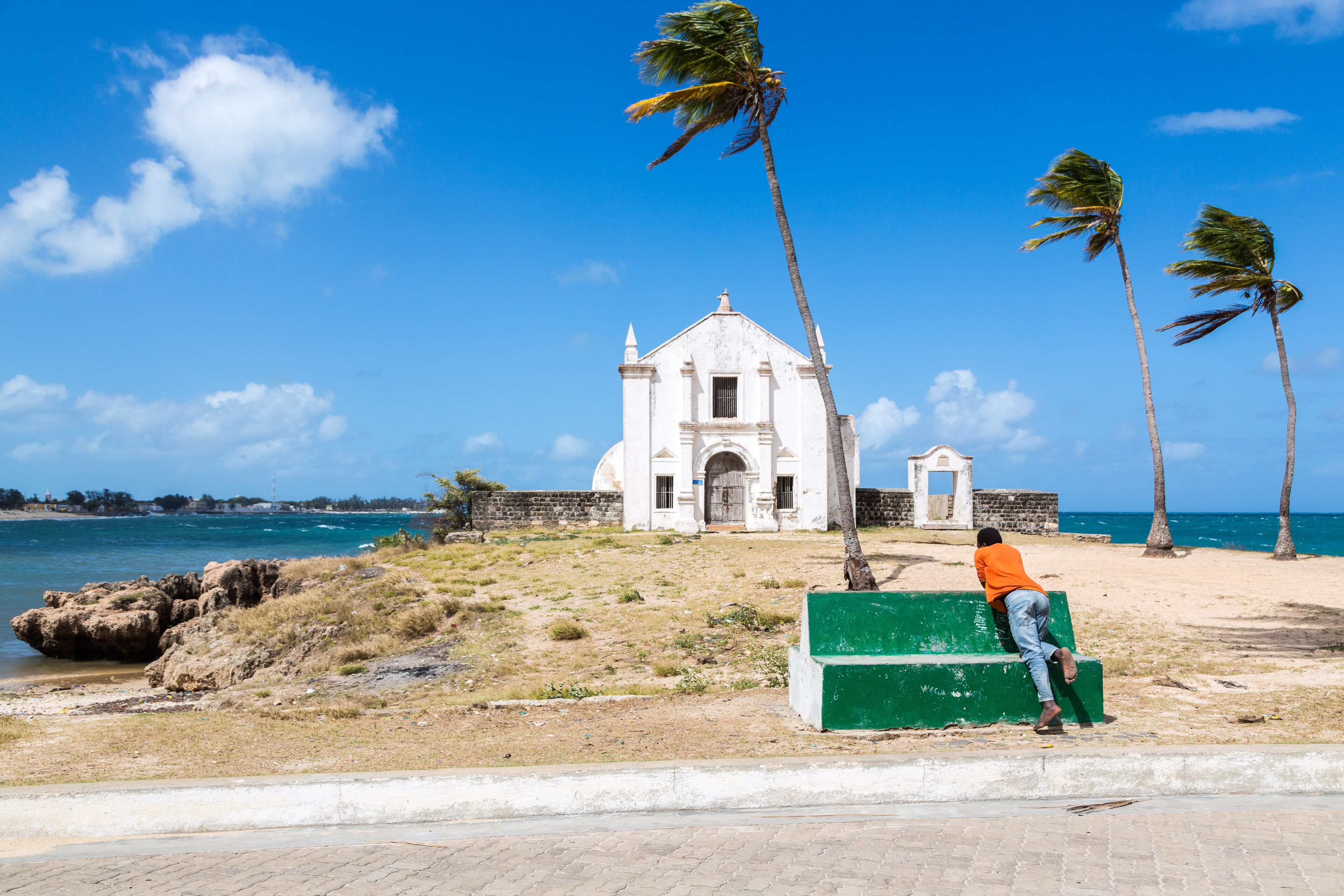 A white church with a bell tower, palm trees, and a beach.