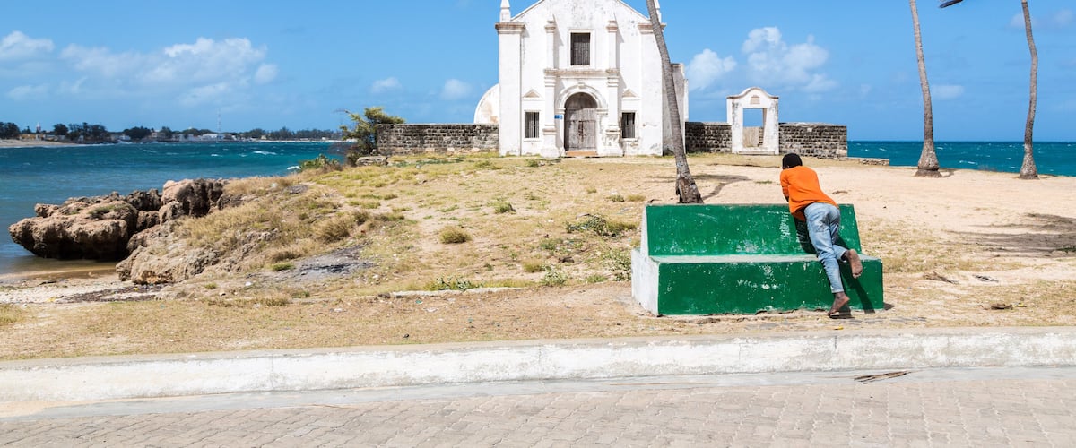 A white church with a bell tower, palm trees, and a beach.