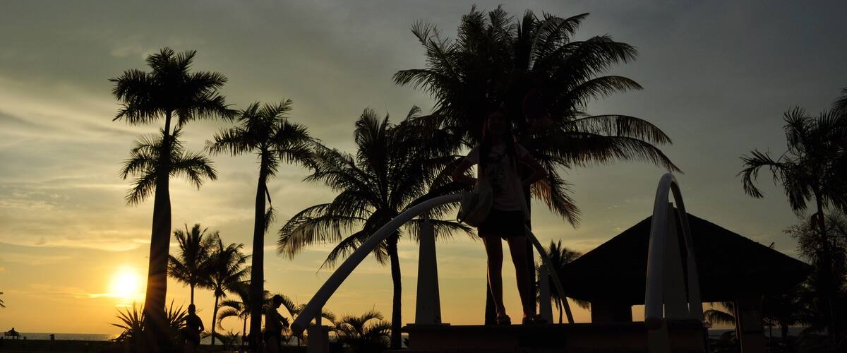 A sunset over a beach with palm trees and a pool.