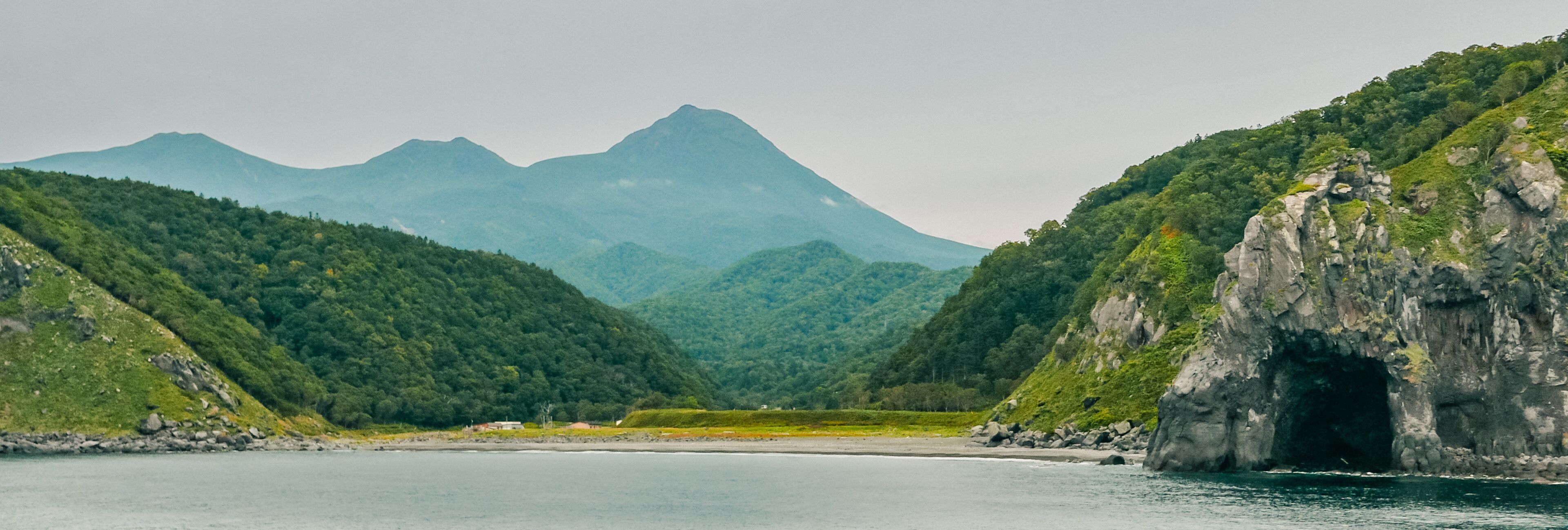 A coastal landscape with a mountain range in the background and a rocky cliff on the right.