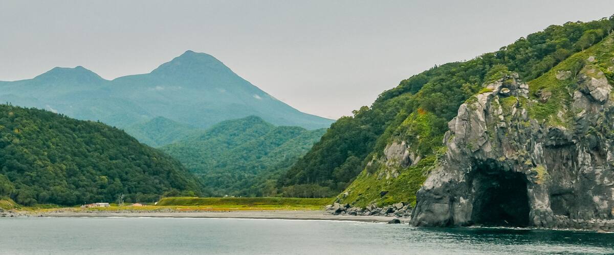 A coastal landscape with a mountain range in the background and a rocky cliff on the right.
