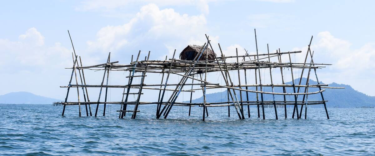 A bamboo raft with a thatched roof floating on calm water.