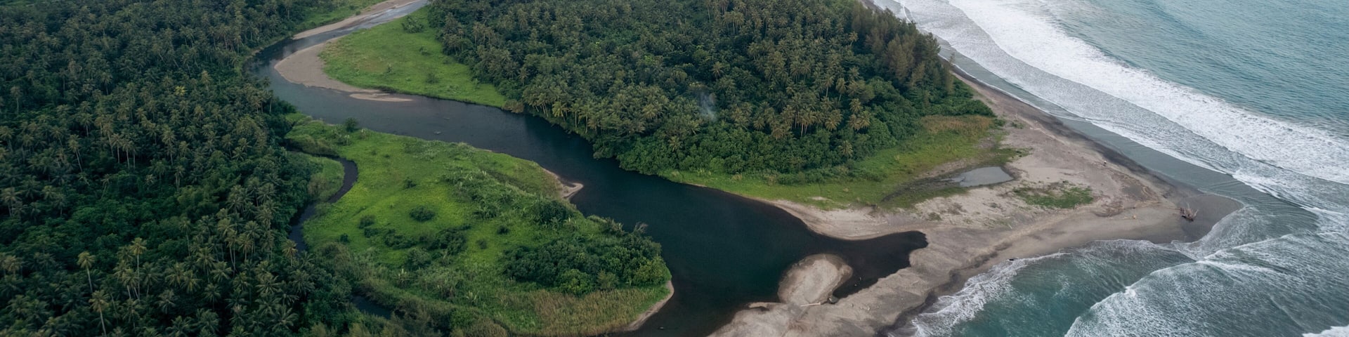 Aerial view of lush green coastline, river meandering through dense forest to sandy beach. South Nias, North Sumatra, Indonesia