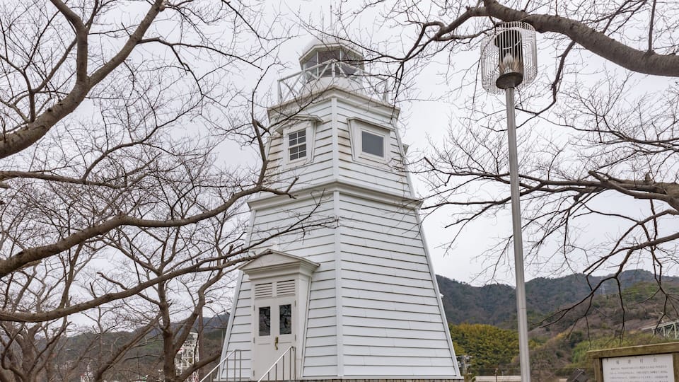A white tower with a stone base, surrounded by bare trees and a mountainous backdrop.