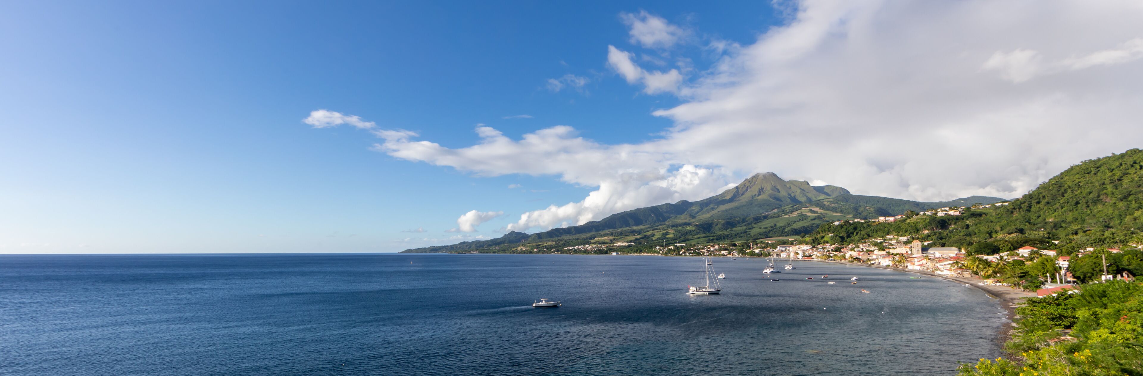 A coastal town with a mountain in the background, boats on the water, and a clear sky.