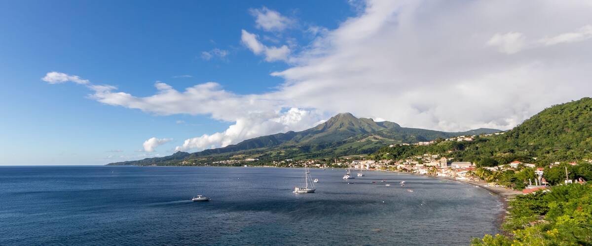A coastal town with a mountain in the background, boats on the water, and a clear sky.
