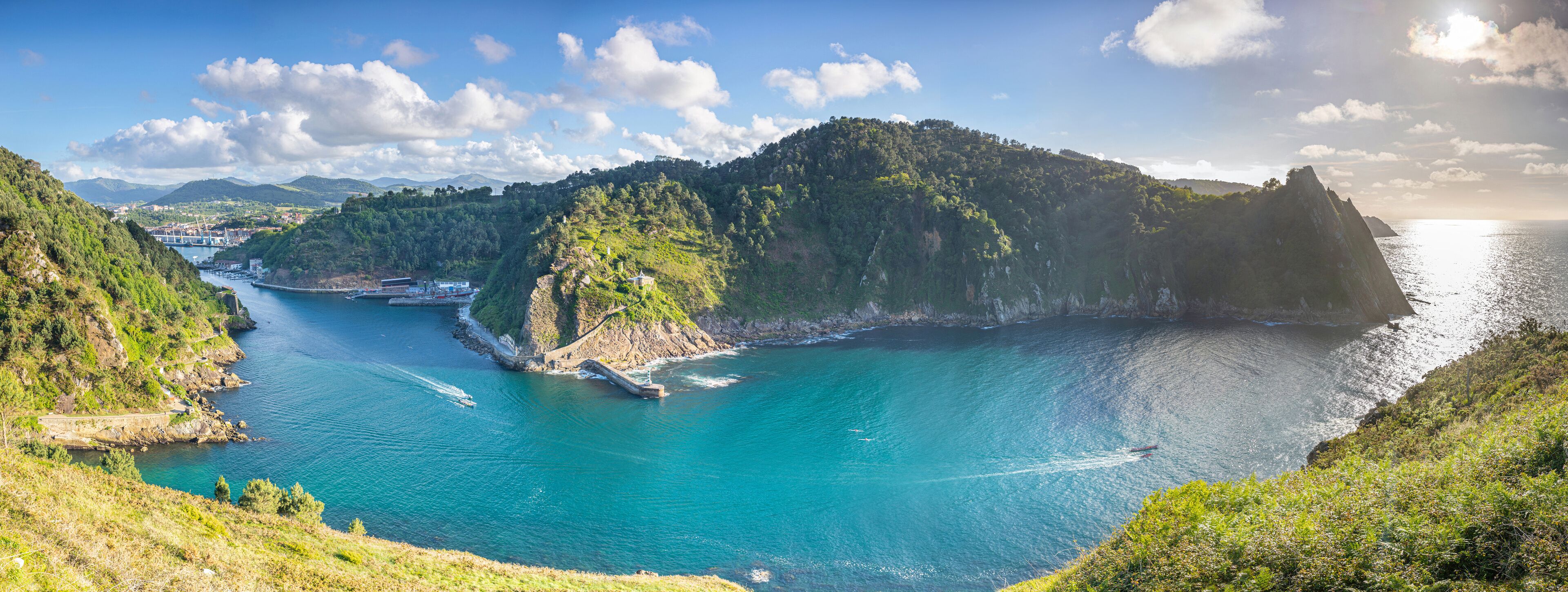 A coastal landscape with a clear blue sea, a small island, and a mountainous backdrop.