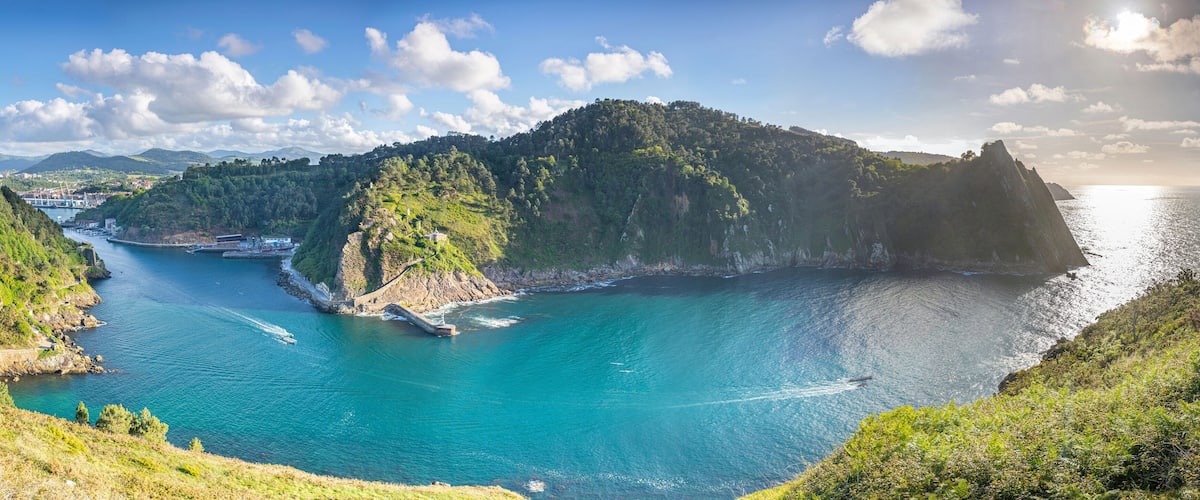 A coastal landscape with a clear blue sea, a small island, and a mountainous backdrop.