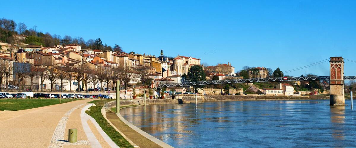 A riverside walkway with a bridge and buildings in the background.