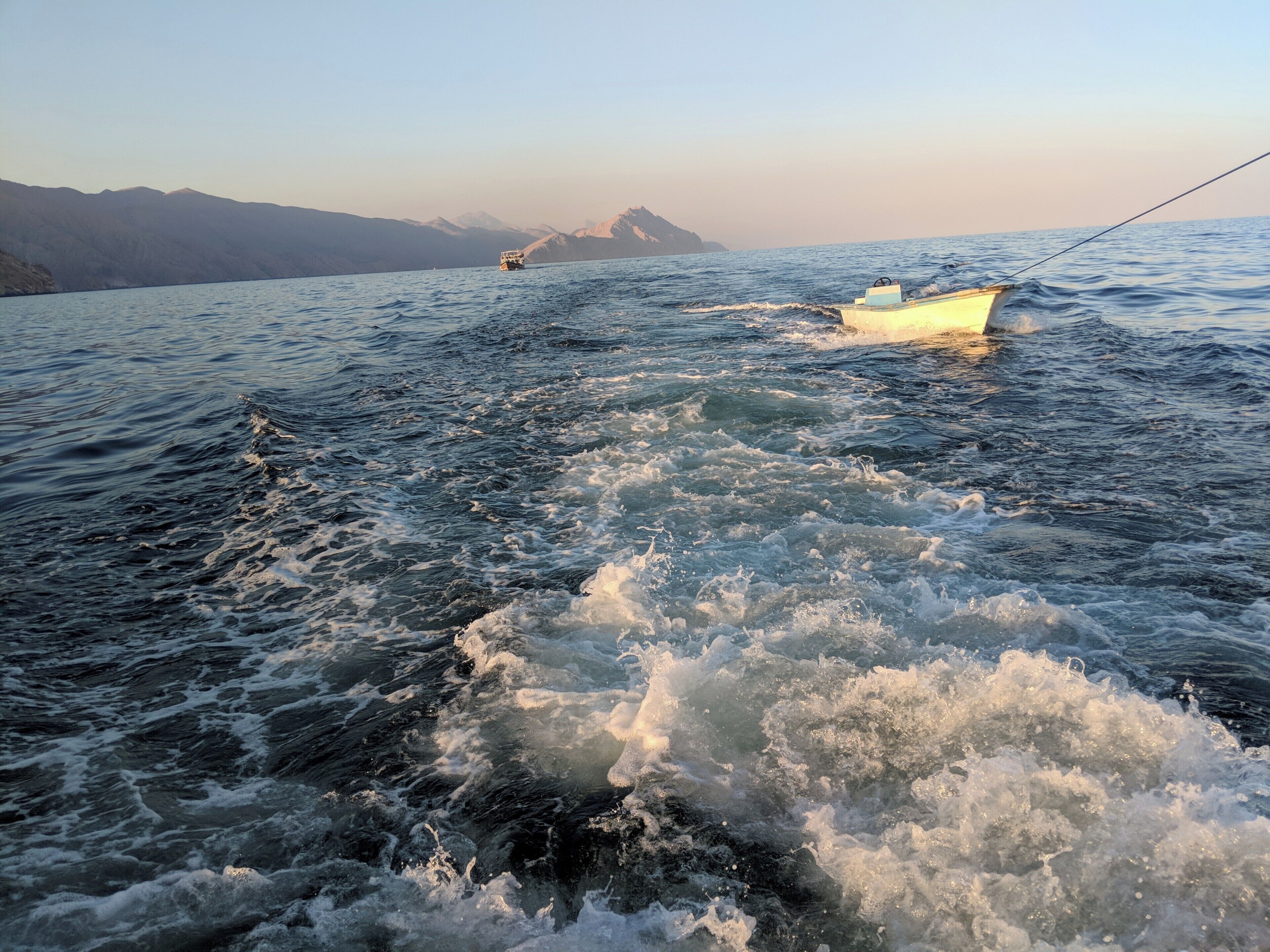 A boat on a body of water with waves and mountains in the background.