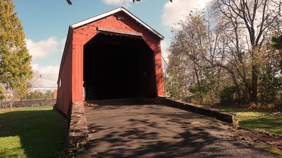 A red covered bridge with a stone base and a sign on the roof.