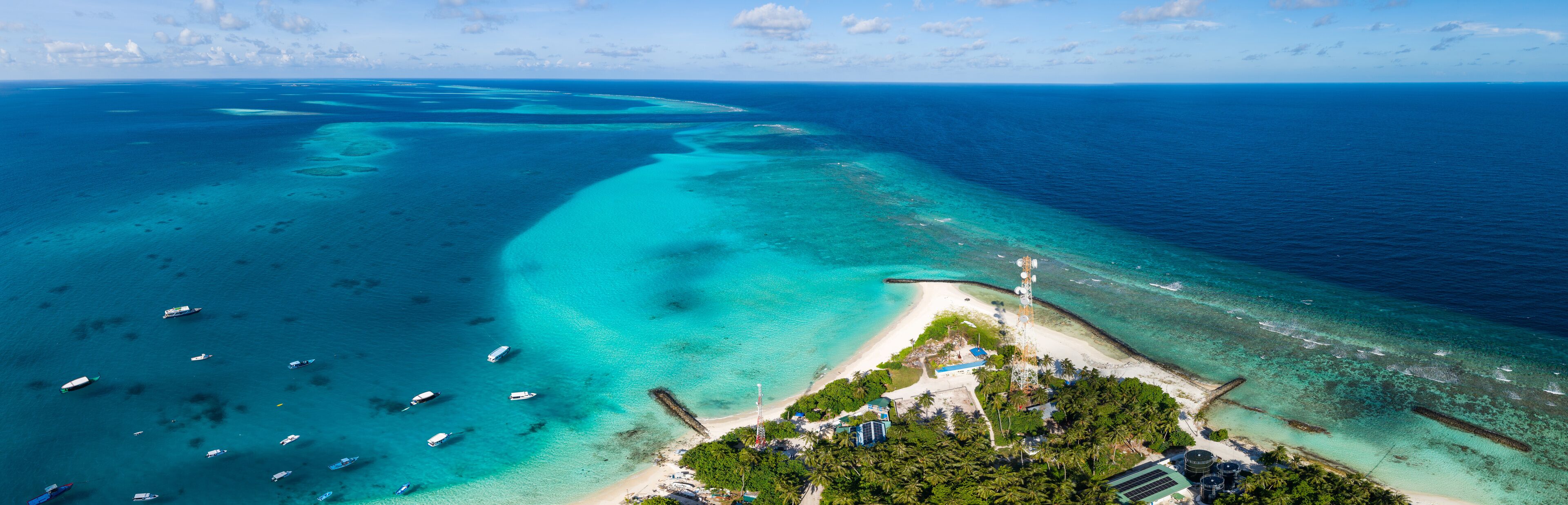 An aerial view of a tropical island with clear turquoise waters, a sandy beach, and several boats.