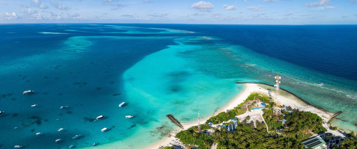 An aerial view of a tropical island with clear turquoise waters, a sandy beach, and several boats.