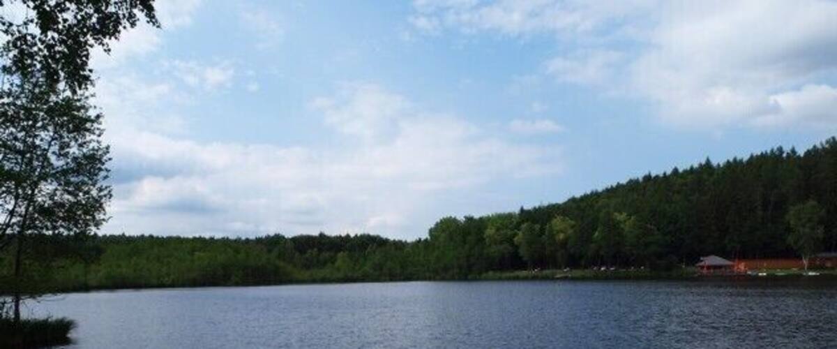 A calm lake surrounded by dense forest and a small building on the right.