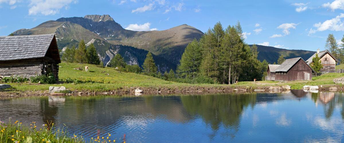 A serene lakeside village with wooden houses, a clear sky, and mountains in the background.