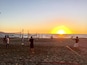 Un match de volleyball de plage au coucher du soleil, avec des joueurs et un filet de volleyball.