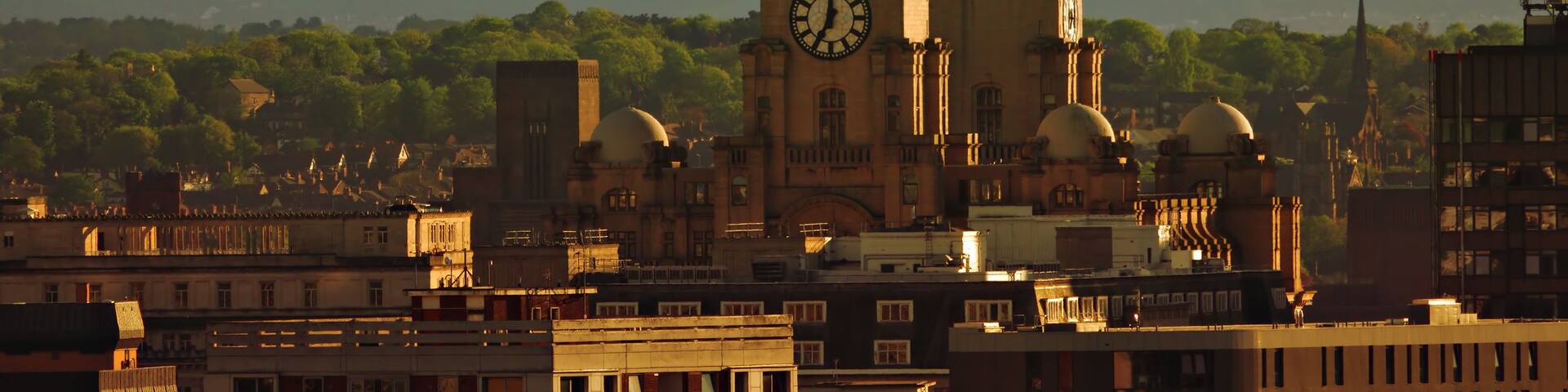 A historic cathedral with twin towers and a large clock, set against a backdrop of a cityscape and distant hills.