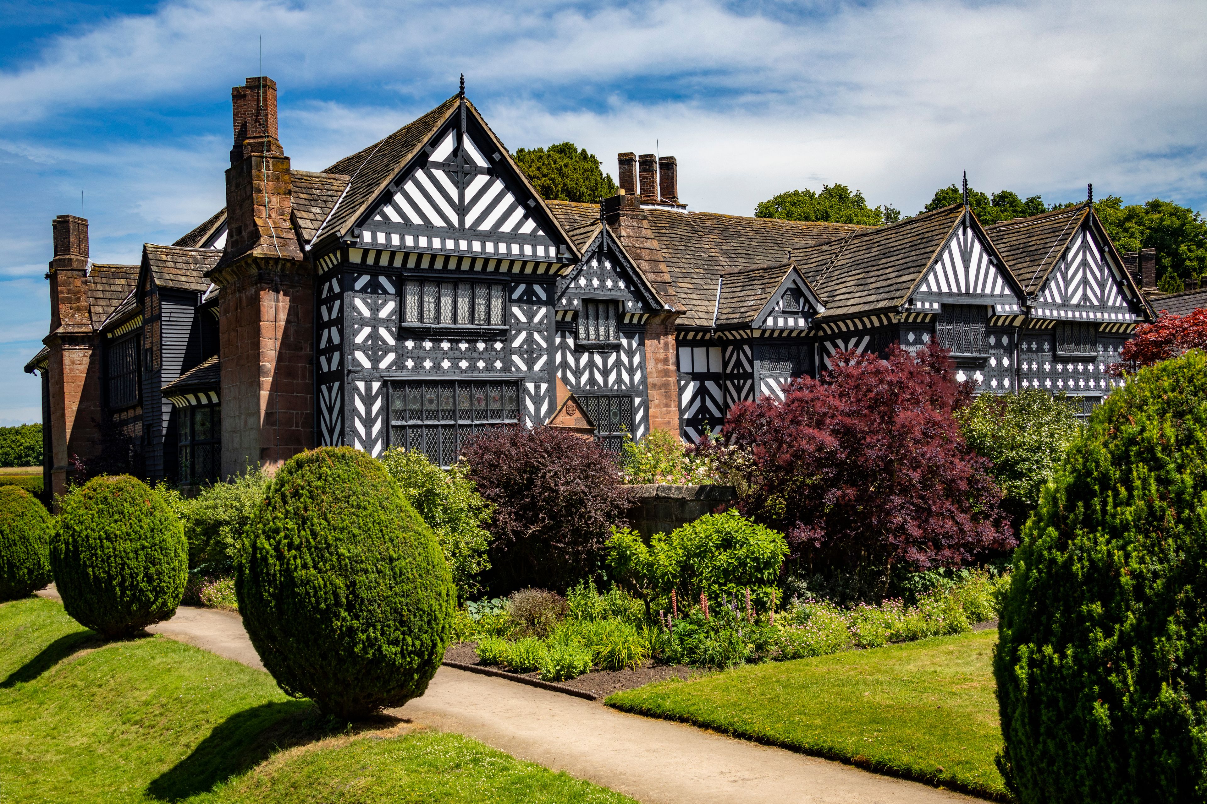 Una mansión de estilo Tudor con un jardín cuidado y un cielo azul despejado.