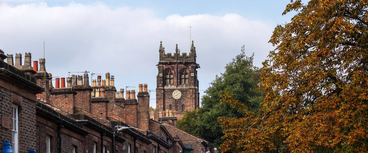 A historic brick building with a clock tower, surrounded by trees with autumn leaves.