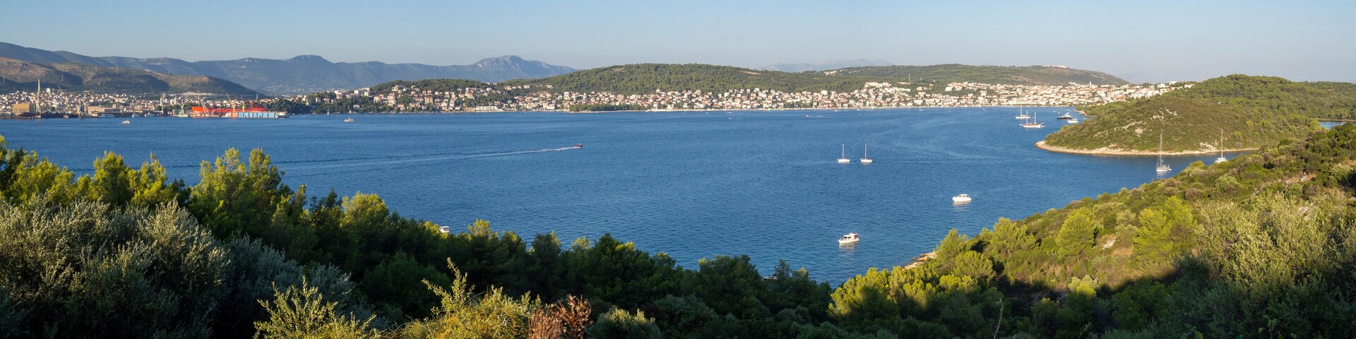 A coastal town with a bay, boats, and a mountainous backdrop.
